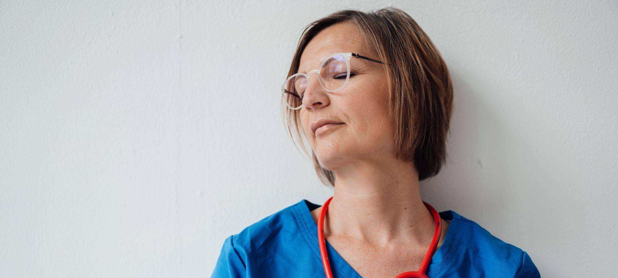 Eine Ärztin lehnt mit geschlossenen Augen an der Wand