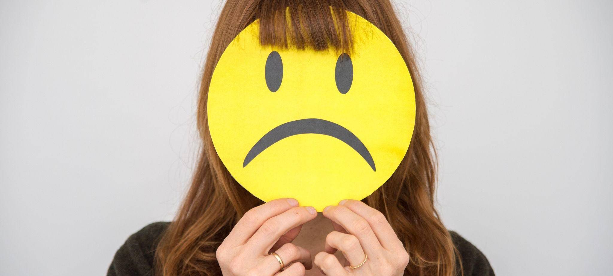 Eine Frau hält sich ein trauriges Smiley vor ihr Gesicht