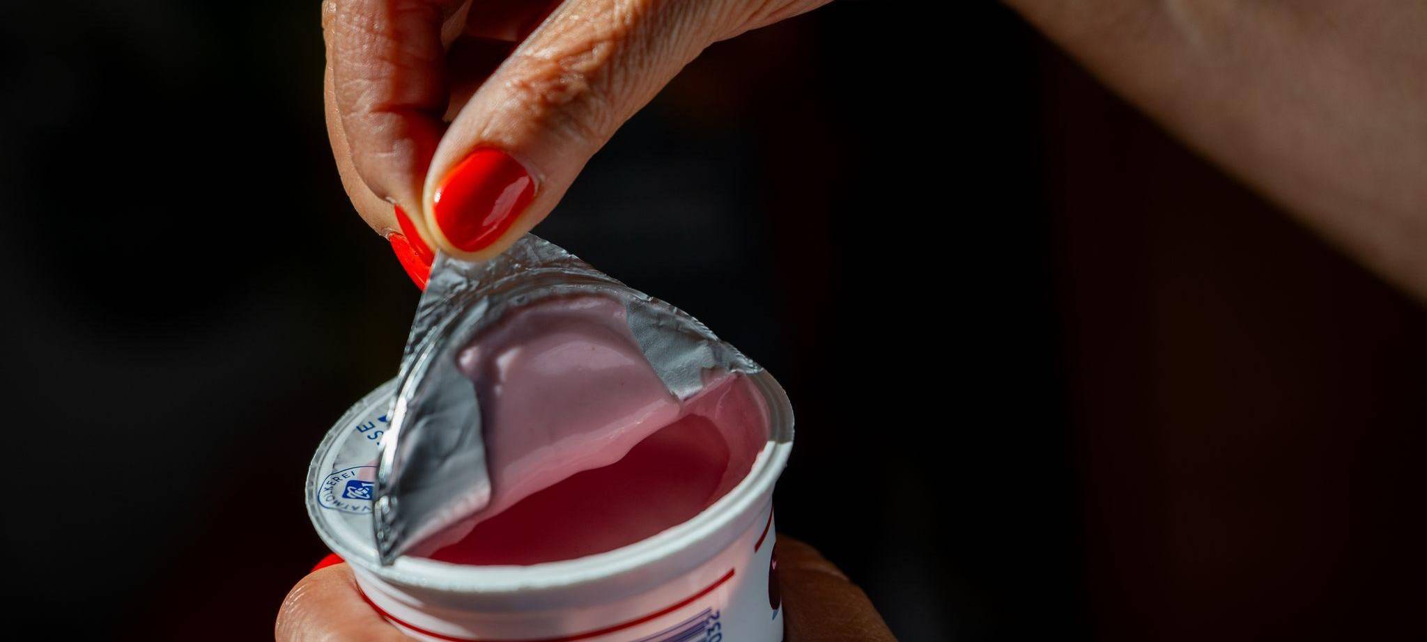 Eine Frau öffnet einen Becher Kirschjoghurt